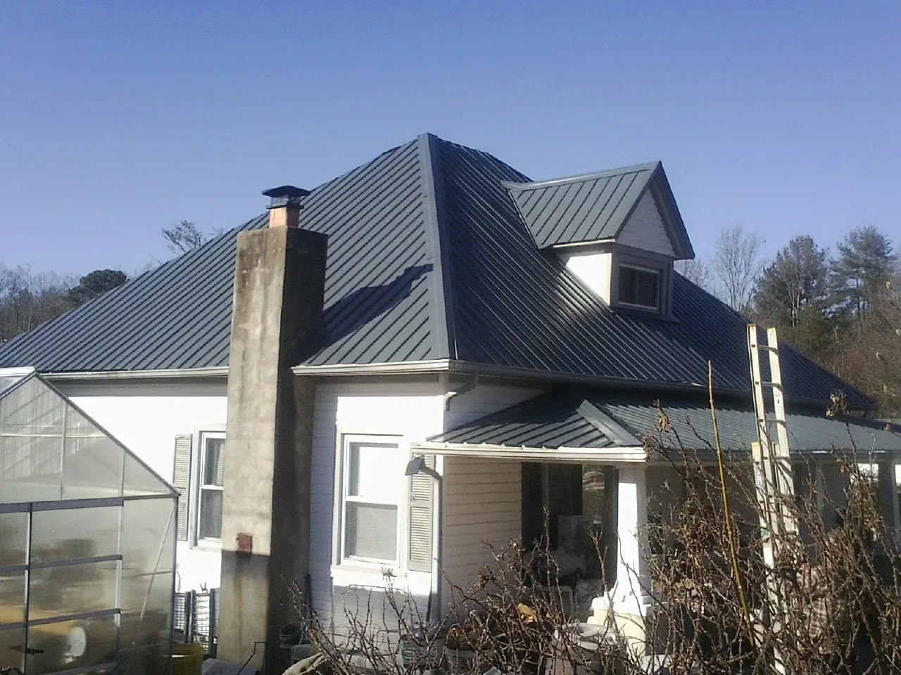 Dark blue standing seam metal roof on a white farmhouse with dormer — Slate & Tile Roof Repair by Roofing Brothers in Manitowoc