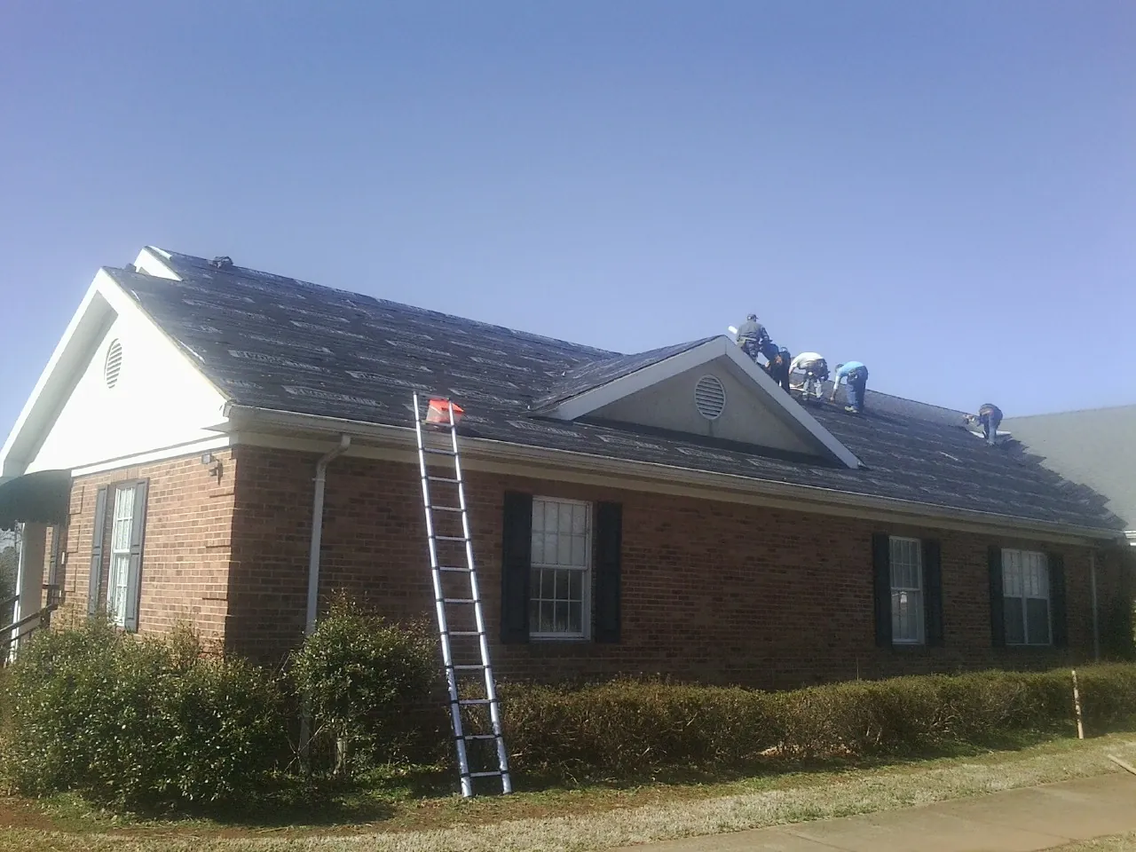 Crew tearing shingles off a brick ranch roof with a ladder set — Emergency Roof Repair work by our crew in Manitowoc