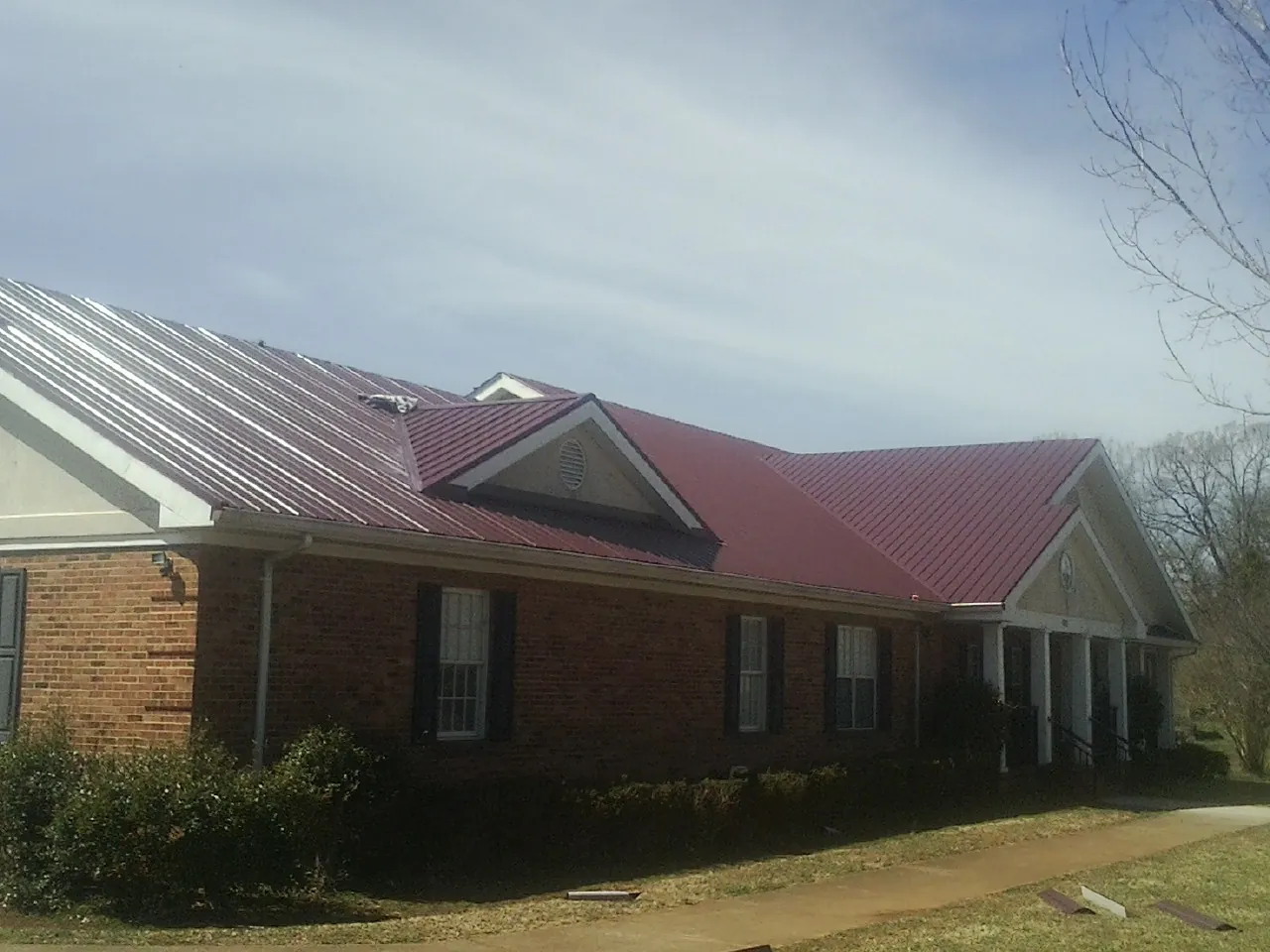 Red metal roof with gabled entries on a long brick building, from a Hail Damage Roof Repair job in Manitowoc