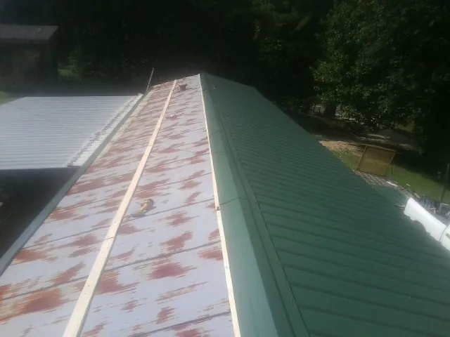 Old rusted panels beside newly installed green metal roofing — Wind Damage Roof Repair by Roofing Brothers in Manitowoc