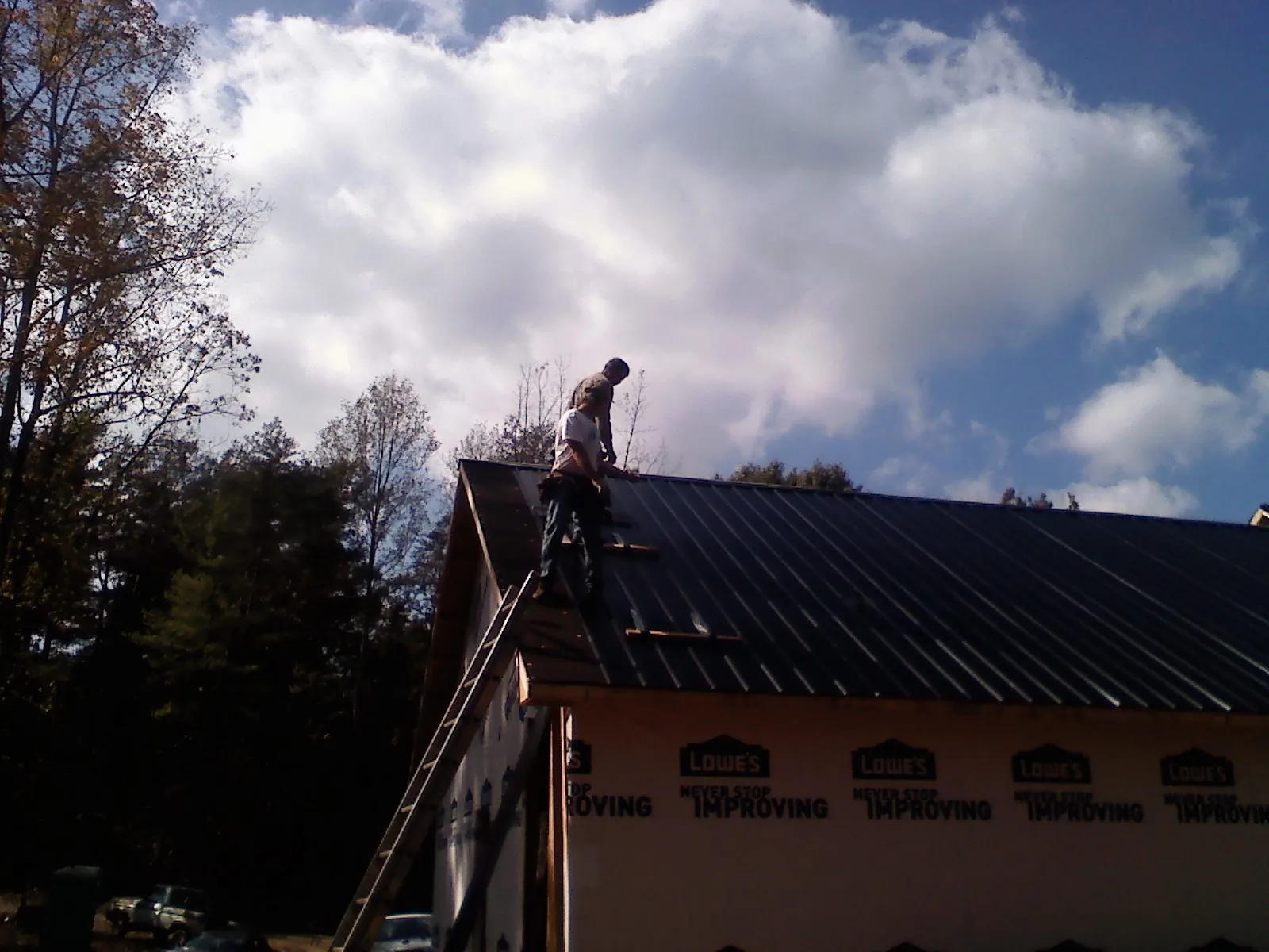 Roofer fastening dark metal panels high against a cloudy sky, from a Roof Inspection job in Manitowoc