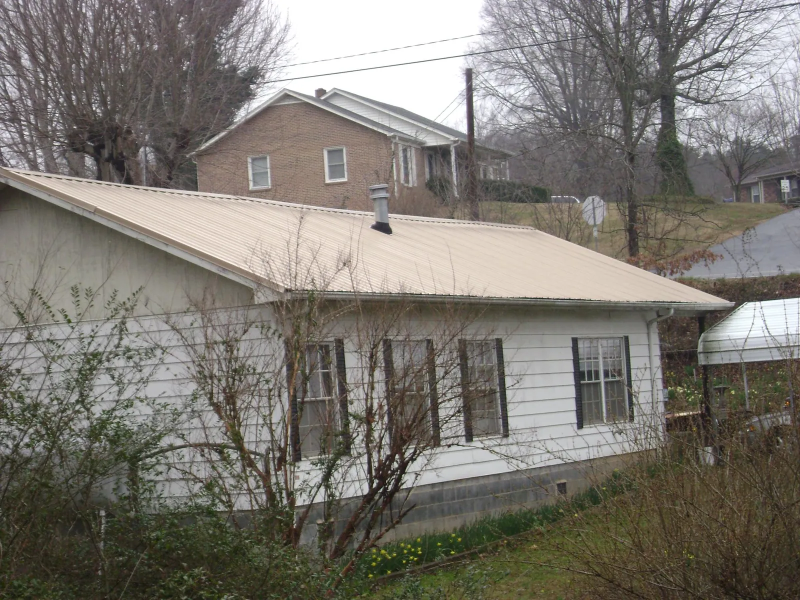 Tan metal roof on a white sided house set into a hillside — Commercial Roofing by Roofing Brothers in Manitowoc